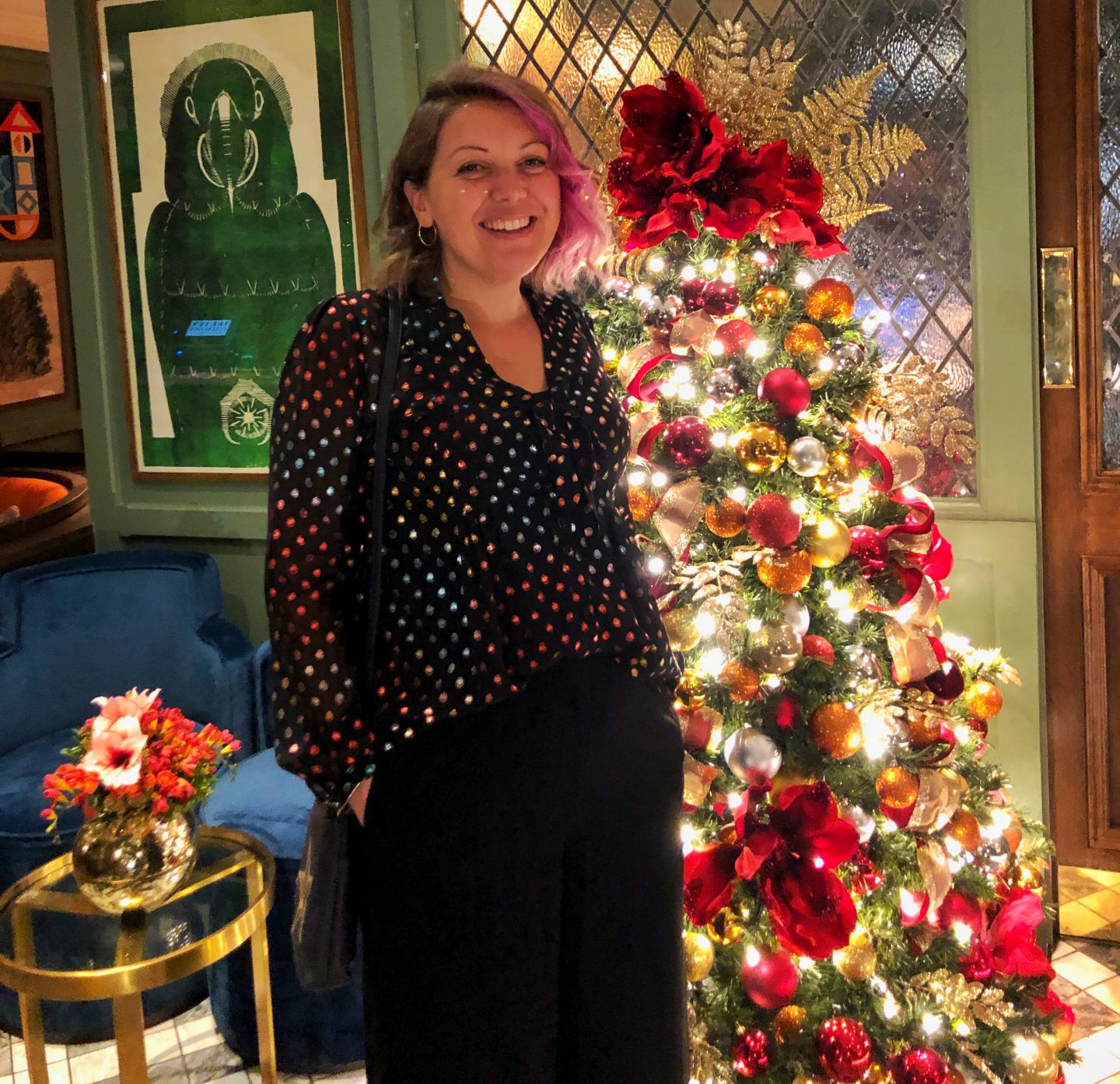 Me, standing by an ornately decorated red and gold tree in the Ivy Cheltenham.