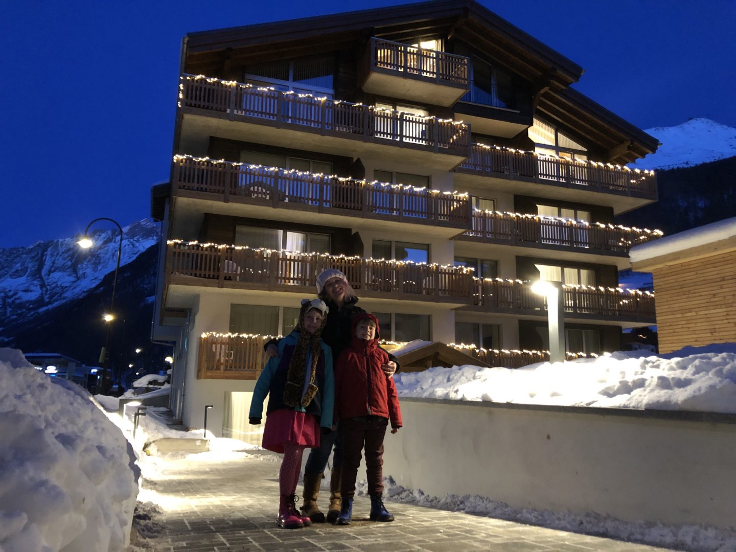 Myself and the children standing outside the Naco Apartments in Zermatt with all the balconies lit up with fairy lights.