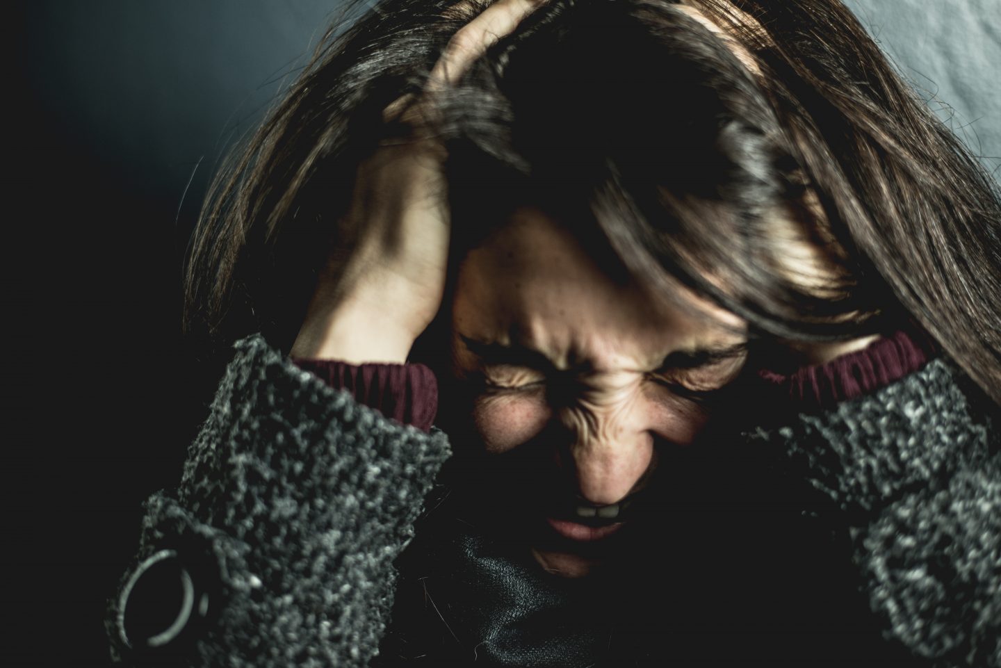 Stock image of a dark haired lady clutching her head with her face screwed up in pain - accurate visual representative of migraines.