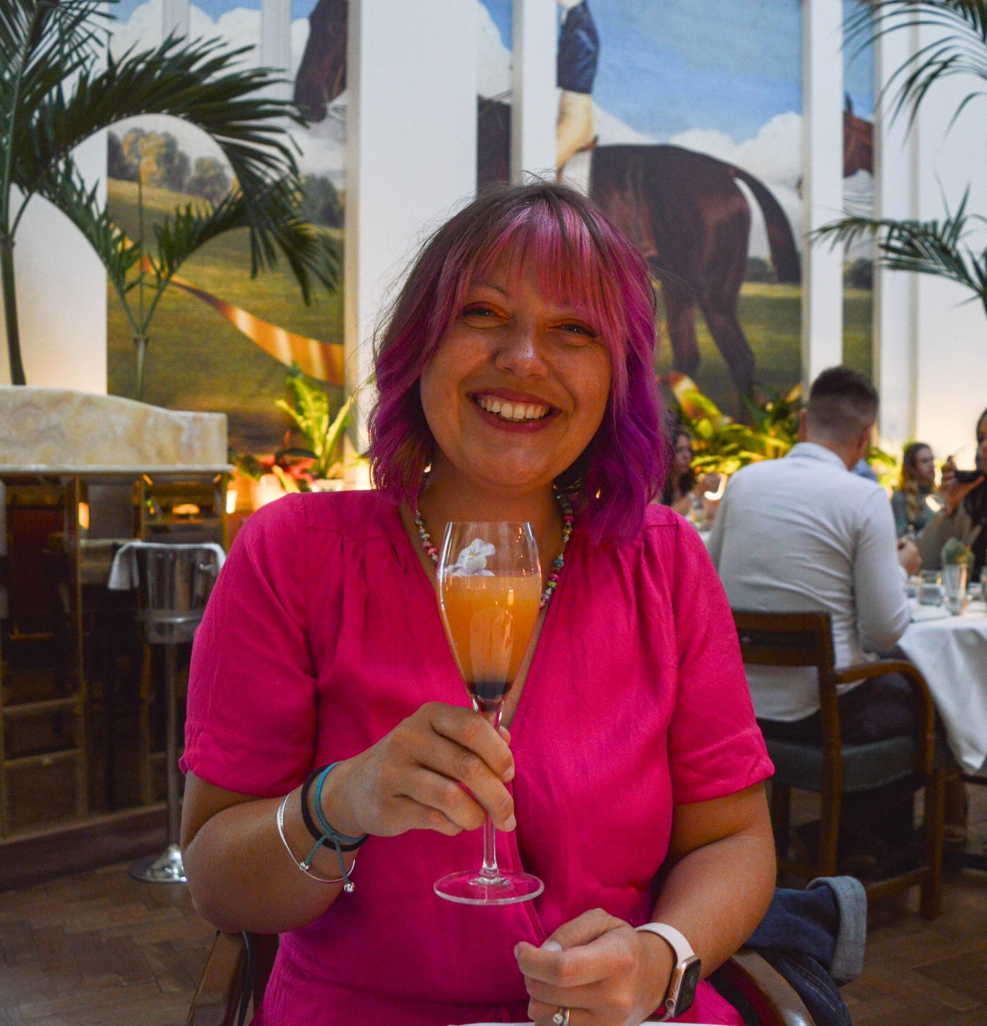 Woman with pink hair sits and enjoys a cocktail.