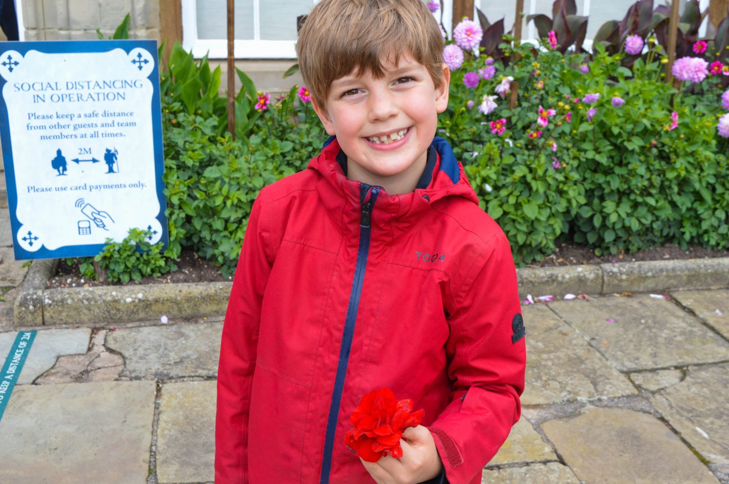 My son, smiling in front of a social distancing sign at Warwick Castle.