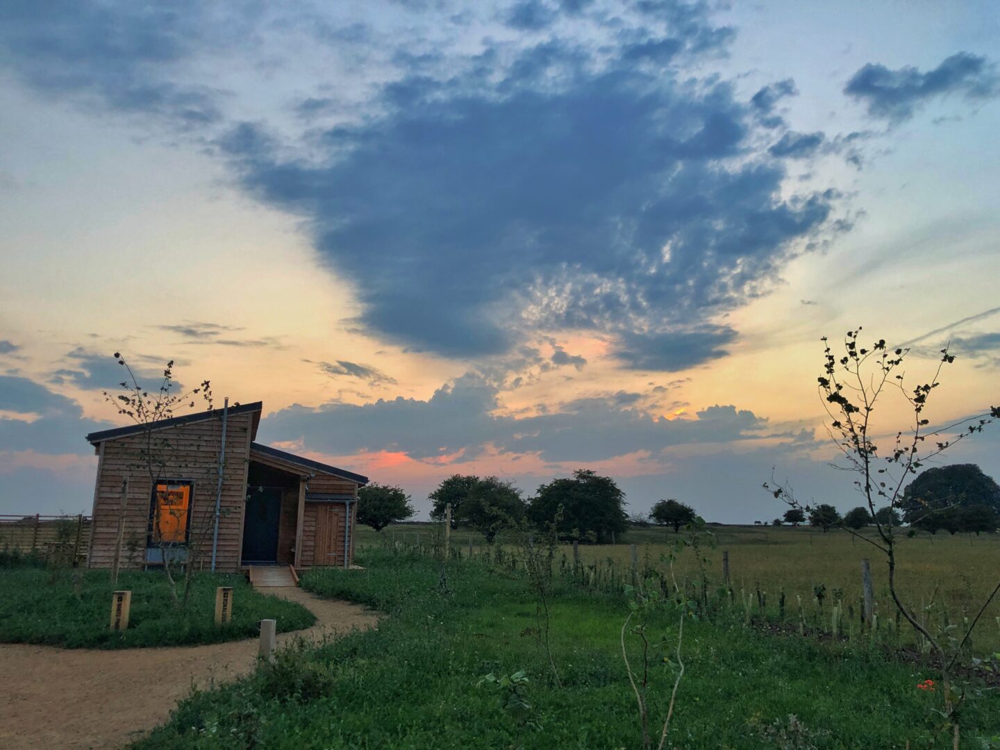 The Sunset Lodges at The Cotswold Farm Park with a very dramatic sunset behind them.