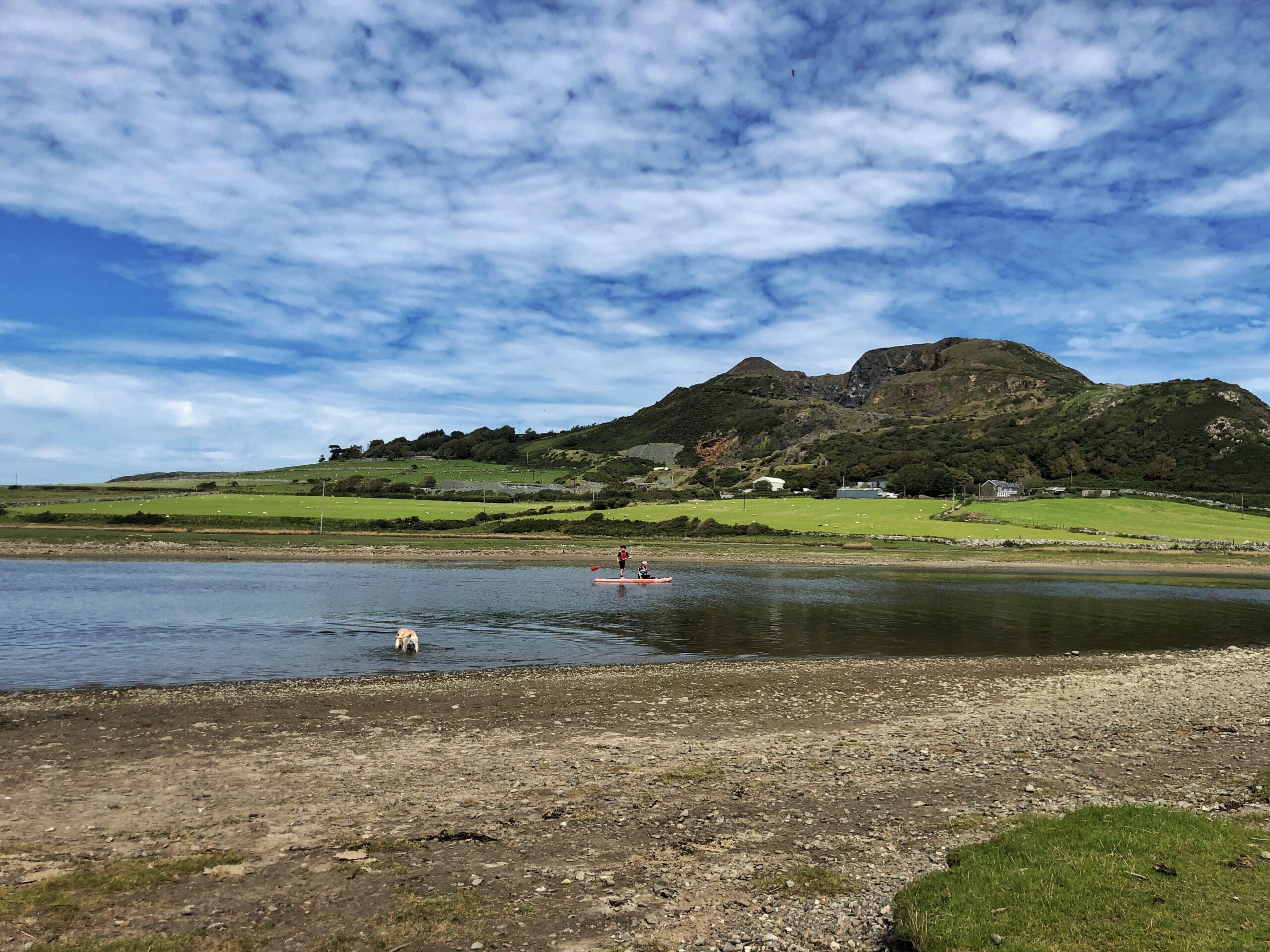 A stunning view of a mountain and river with two children on a SUP.