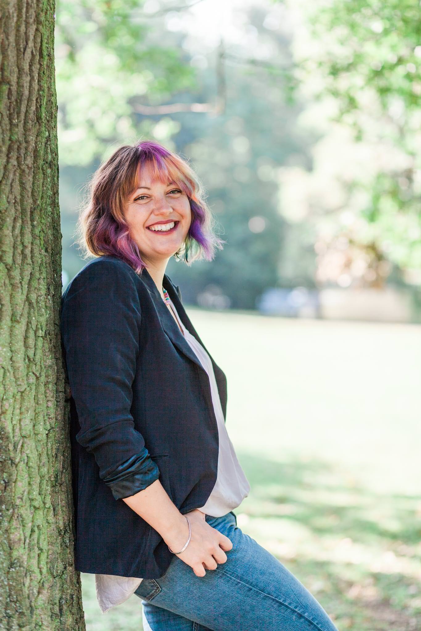 A photo of me leaning against a tree and smiling to the camera. I'm so much happier now that my ADHD and Rejection Sensitive Dysphoria are under control.
